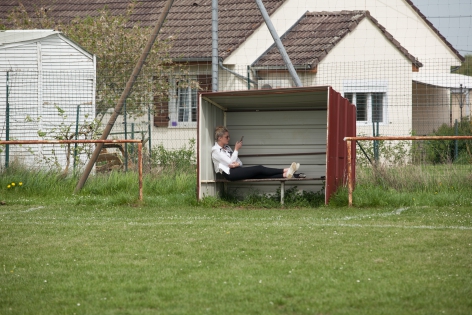 A player's wife waits on the bench for players to come out of the locker room. In Nievre, department where many communes and villages are affected by rural desertification, football remains an activity that maintains social ties. In Narcy, a village of 530 inhabitants, a small stadium welcomes more than seventy licensees throughout the year, from the youngest to the oldest. A real place to meet and learn where friends and families of FC Narcy players converge every weekend for a game in the countryside. Narcy, France - 22 april 2018.
Une femme de joueur attend sur le banc de touche que les joueurs sortent du vestiaire.  Dans la Ni